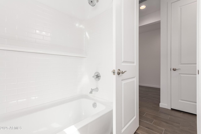 bathroom with washtub / shower combination, baseboards, and wood finished floors