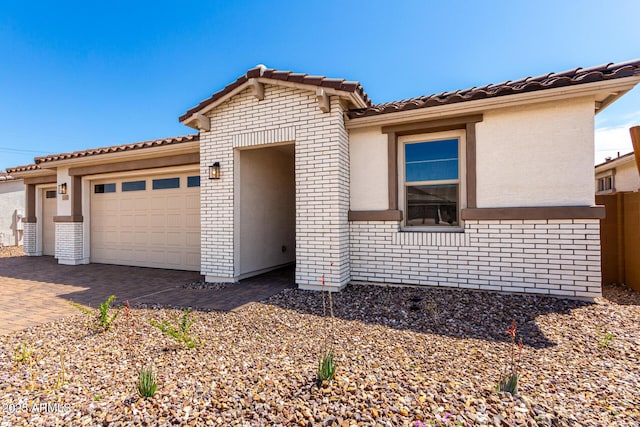 single story home featuring stucco siding, decorative driveway, brick siding, a tile roof, and a garage