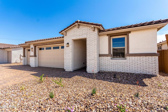 single story home featuring brick siding, an attached garage, decorative driveway, and stucco siding