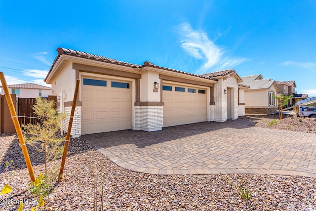 mediterranean / spanish house with stucco siding, decorative driveway, fence, a tile roof, and an attached garage