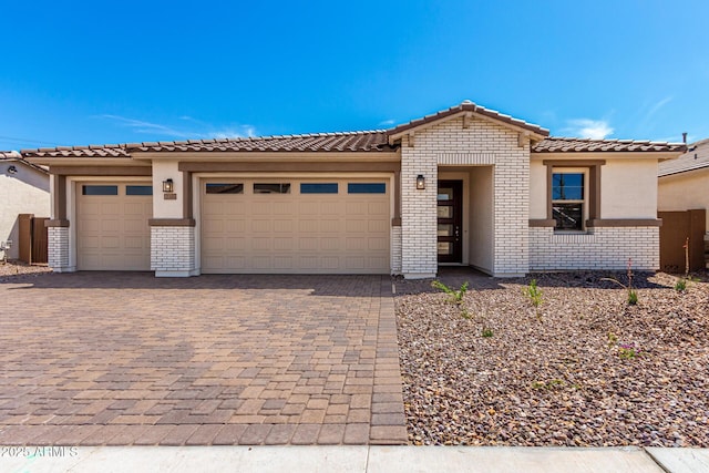 view of front facade with a tiled roof, stucco siding, decorative driveway, brick siding, and a garage