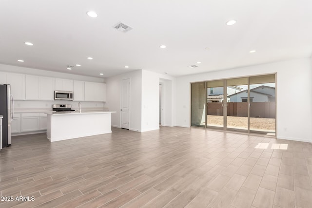 unfurnished living room featuring light wood-type flooring, visible vents, recessed lighting, a sink, and baseboards