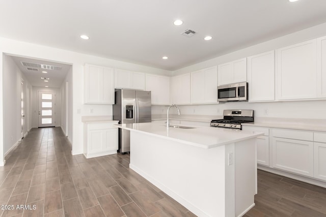 kitchen with white cabinetry, a center island with sink, appliances with stainless steel finishes, a sink, and wood finished floors