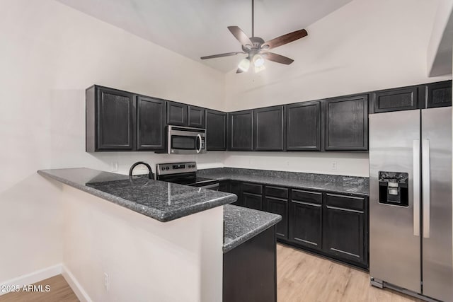 kitchen featuring appliances with stainless steel finishes, dark cabinets, a ceiling fan, dark stone counters, and a peninsula