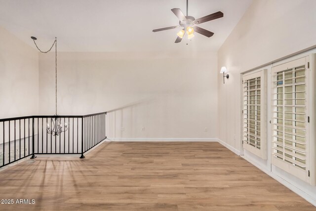 spare room with a ceiling fan, wood finished floors, a chandelier, lofted ceiling, and baseboards