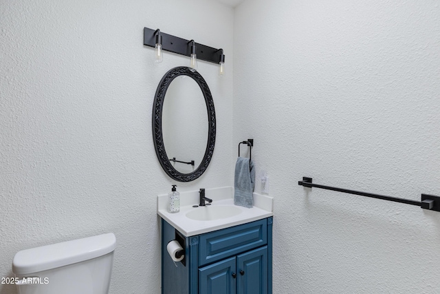 bathroom with toilet, vanity, and a textured wall