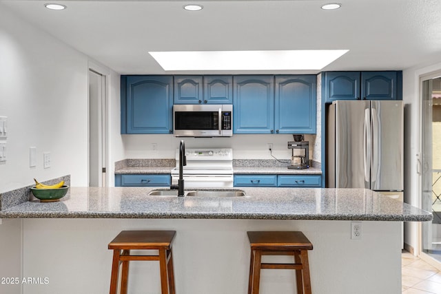 kitchen with blue cabinetry, stainless steel appliances, a kitchen bar, and a sink