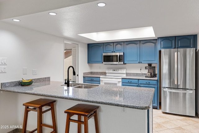 kitchen with a peninsula, blue cabinetry, appliances with stainless steel finishes, and a sink