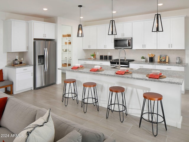 kitchen featuring white cabinetry, appliances with stainless steel finishes, hanging light fixtures, and an island with sink