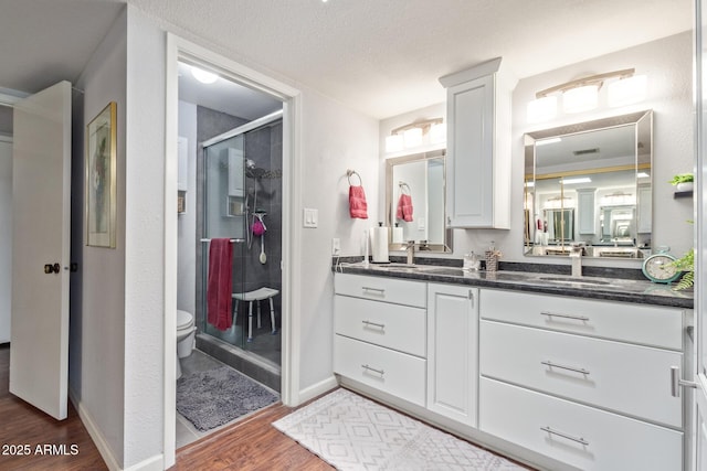 bathroom with hardwood / wood-style flooring, a shower with door, vanity, a textured ceiling, and toilet