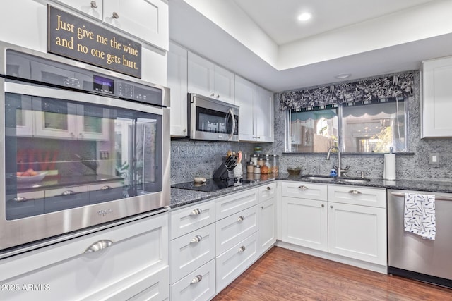 kitchen featuring sink, white cabinetry, dark stone countertops, dark hardwood / wood-style flooring, and stainless steel appliances