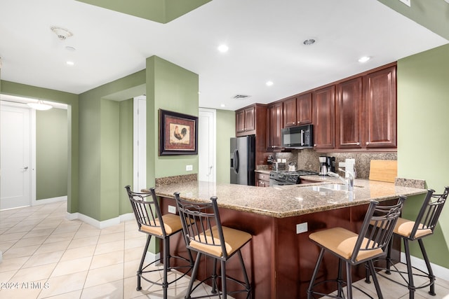 kitchen featuring kitchen peninsula, appliances with stainless steel finishes, decorative backsplash, and a breakfast bar