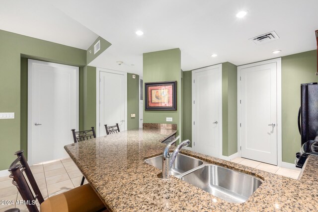 kitchen with sink, kitchen peninsula, a kitchen breakfast bar, light stone countertops, and light tile patterned floors