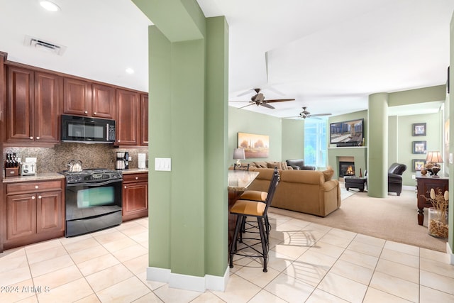 kitchen featuring light carpet, black appliances, tasteful backsplash, ceiling fan, and a breakfast bar area