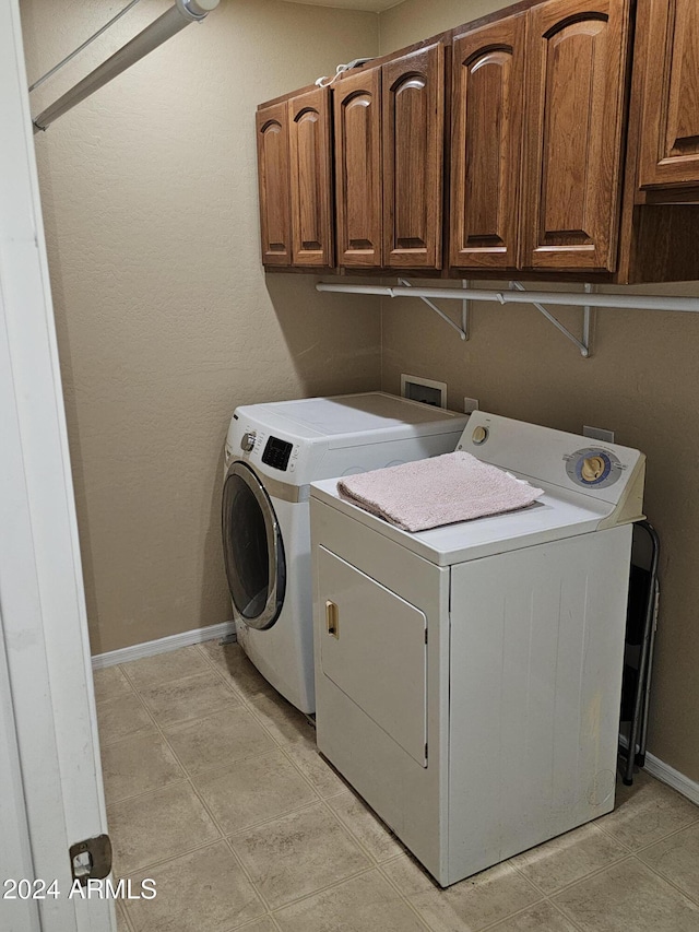 laundry area with washing machine and clothes dryer, light tile patterned floors, and cabinets