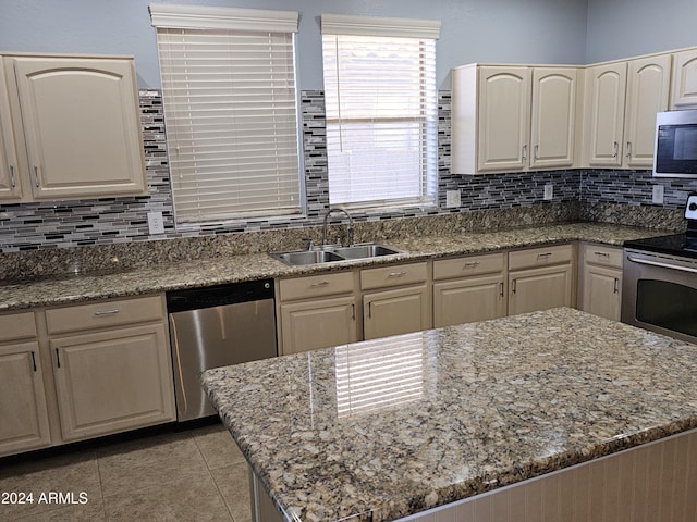 kitchen featuring decorative backsplash, light stone counters, sink, and appliances with stainless steel finishes