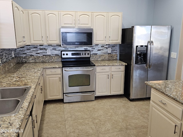 kitchen featuring sink, tasteful backsplash, light stone counters, light tile patterned floors, and appliances with stainless steel finishes