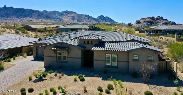 view of front facade featuring fence, stucco siding, a tiled roof, decorative driveway, and a mountain view