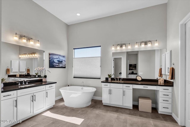 full bath with a sink, a freestanding tub, baseboards, and two vanities