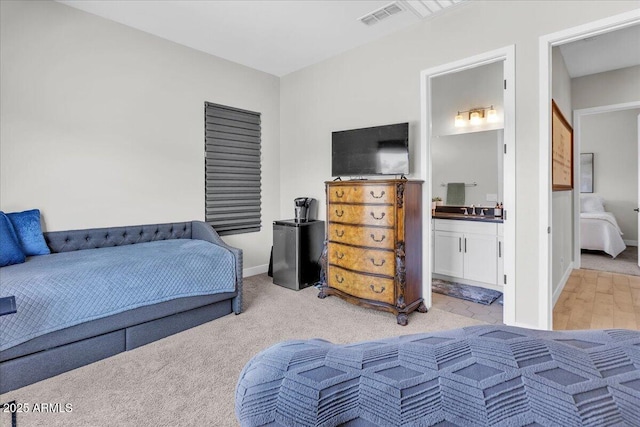 bedroom with light colored carpet, visible vents, ensuite bathroom, and baseboards