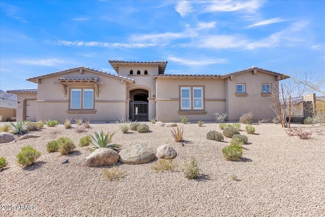 mediterranean / spanish-style house featuring stucco siding, a tiled roof, fence, and a gate