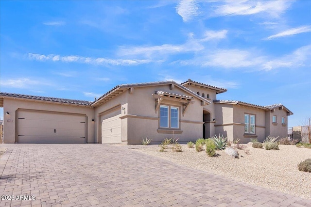 mediterranean / spanish-style house featuring stucco siding, decorative driveway, an attached garage, and a tile roof