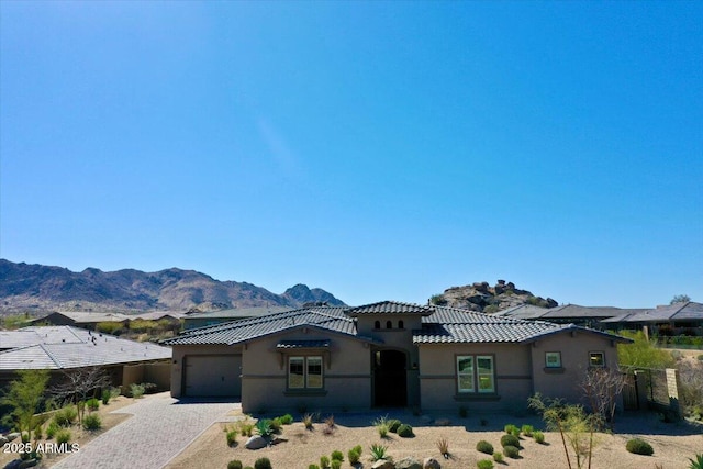 view of front of house featuring stucco siding, decorative driveway, a mountain view, a garage, and a tiled roof