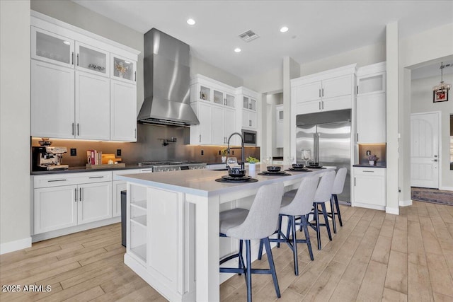 kitchen with visible vents, a sink, light wood-style floors, wall chimney range hood, and built in appliances