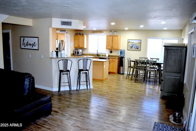 kitchen featuring visible vents, a kitchen bar, wood finished floors, a peninsula, and stainless steel fridge with ice dispenser