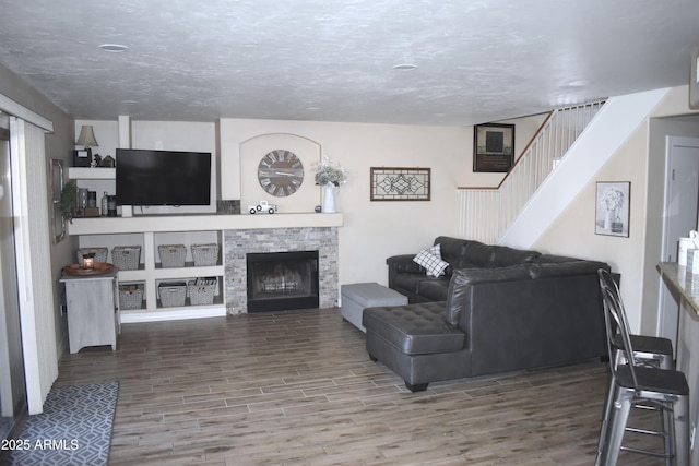 living area with a fireplace, a textured ceiling, stairs, and wood finished floors