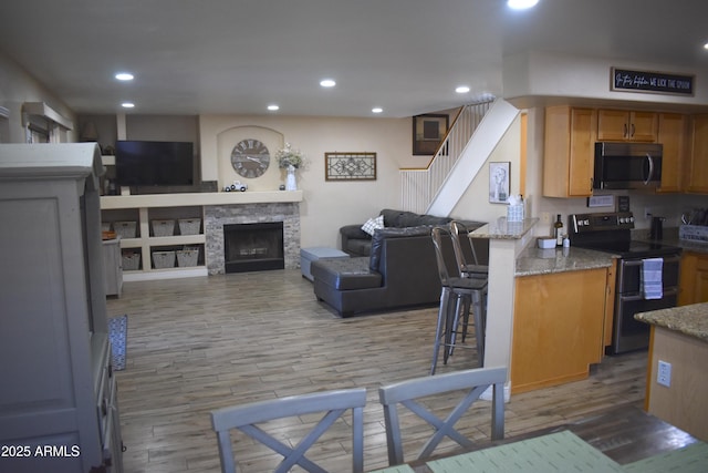 kitchen featuring light wood finished floors, open floor plan, a breakfast bar, light stone counters, and appliances with stainless steel finishes