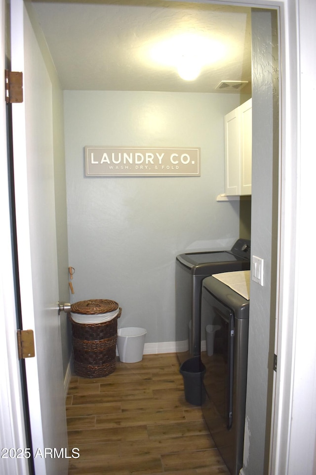 clothes washing area with visible vents, washer and clothes dryer, wood finished floors, cabinet space, and baseboards