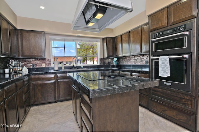 kitchen with dark brown cabinetry, sink, stainless steel double oven, a kitchen island, and exhaust hood