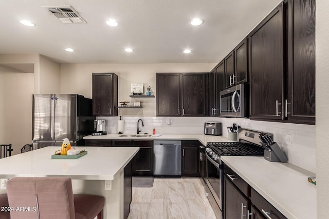 kitchen with a breakfast bar, sink, dark brown cabinets, stainless steel appliances, and backsplash