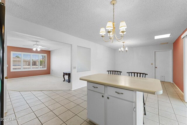 kitchen featuring hanging light fixtures, a textured ceiling, white cabinetry, a breakfast bar, and ceiling fan with notable chandelier