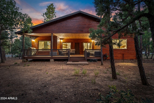 back house at dusk with a porch and a wooden deck