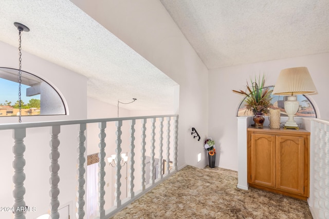 hall featuring carpet, a textured ceiling, and vaulted ceiling