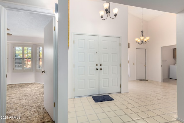 foyer entrance featuring a high ceiling, an inviting chandelier, light colored carpet, a textured ceiling, and washer / dryer