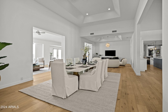 dining area with a towering ceiling, ceiling fan with notable chandelier, light hardwood / wood-style floors, and a raised ceiling