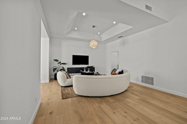 living room featuring a chandelier, light wood-type flooring, and a tray ceiling