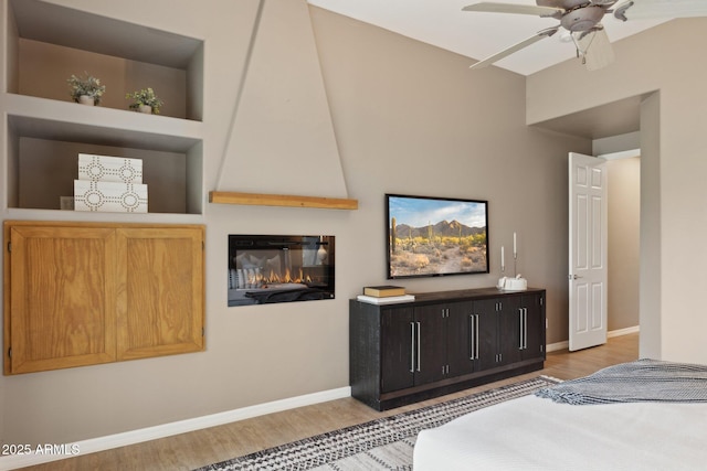 bedroom with baseboards, ceiling fan, light wood-style flooring, and a fireplace