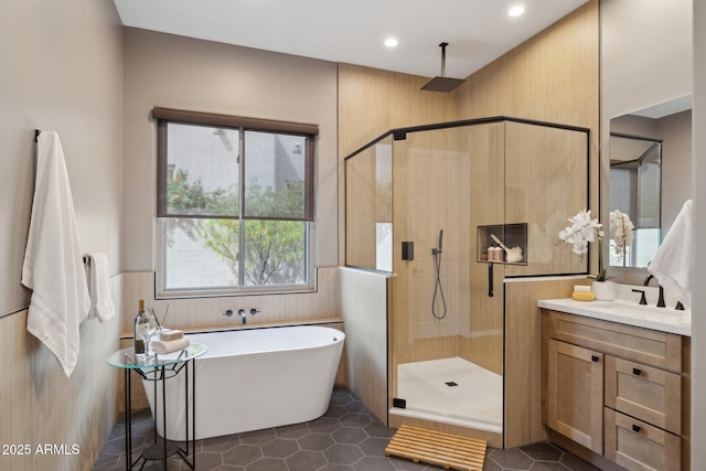 full bathroom with tile patterned flooring, vanity, a wainscoted wall, a soaking tub, and a stall shower
