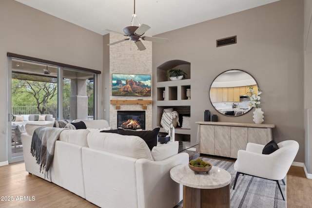 living area featuring visible vents, wood finished floors, baseboards, a large fireplace, and a ceiling fan