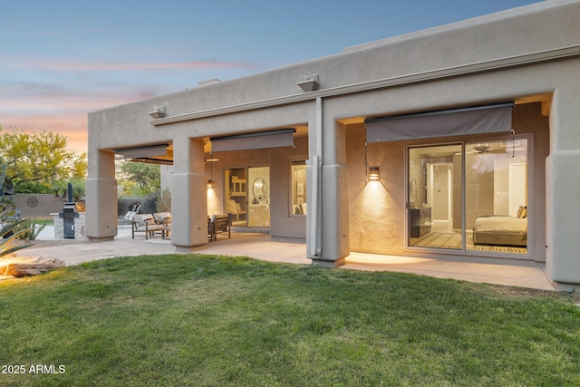 back of house with a lawn, a patio area, and stucco siding