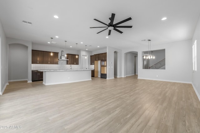 unfurnished living room with light wood-type flooring and ceiling fan with notable chandelier