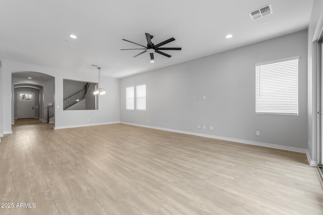 unfurnished living room featuring ceiling fan with notable chandelier and light hardwood / wood-style flooring