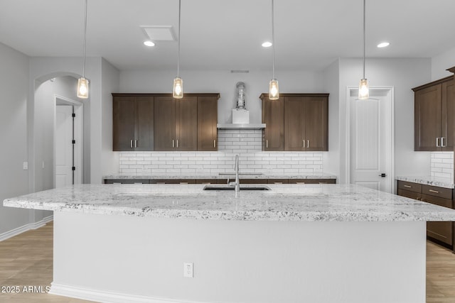 kitchen with decorative light fixtures, dark brown cabinetry, a kitchen island with sink, and tasteful backsplash