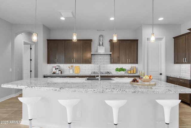 kitchen featuring tasteful backsplash, a kitchen island with sink, light stone counters, and pendant lighting