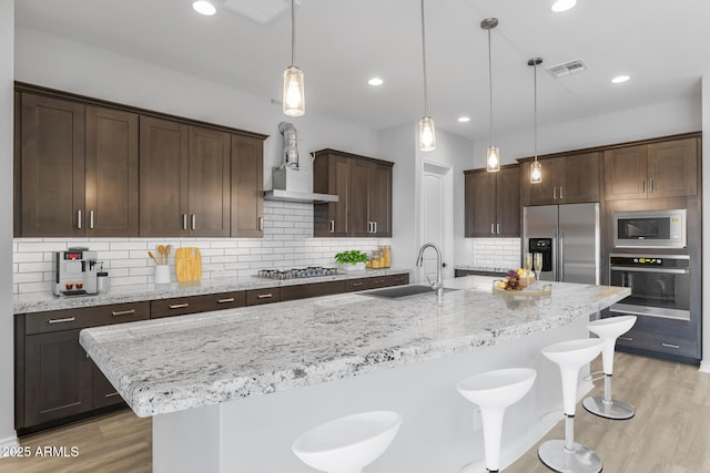 kitchen featuring appliances with stainless steel finishes, tasteful backsplash, sink, hanging light fixtures, and a center island with sink