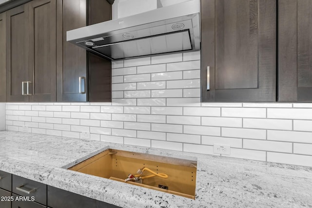 kitchen with wall chimney exhaust hood, dark brown cabinets, and light stone counters